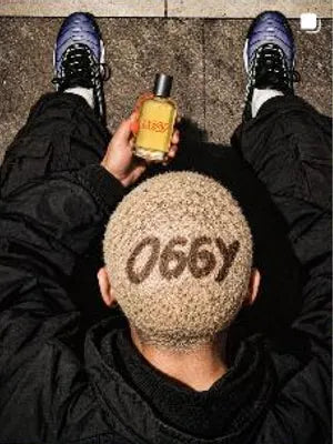 Cabeza rapada con la palabra O66Y y el perfume O66Y en la mano